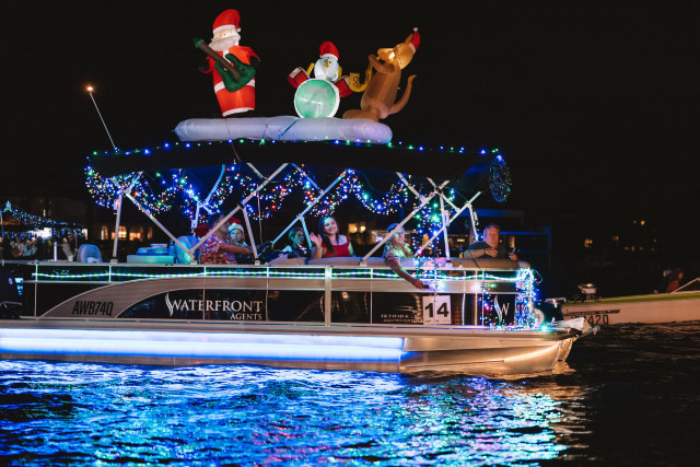 A festively decorated boat adorned with Christmas lights, inflatable Santa, and reindeer floats along the water at a Christmas event on the Sunshine Coast.